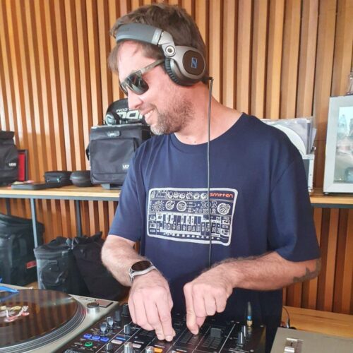 Man wearing Smitten Silver Print TB303 Navy T Shirt riding the volume faders whilst DJing