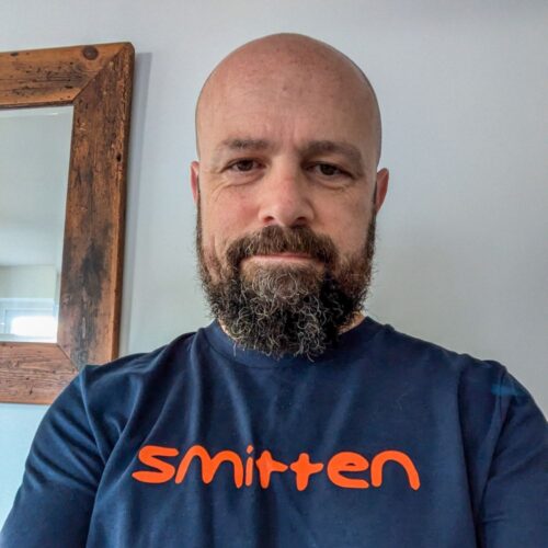 bald man with beard wearing Smitten orange logo navy t-shirt